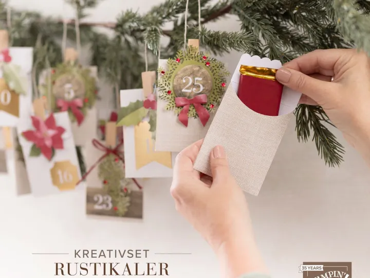 Eine Hand hält einen Adventskalender-Tage-Beutel aus hellem Stoffpapier mit einem roten Umschlag darin, während im Hintergrund an einer Tanne mehrere dekorierte Tagekarten mit Zahlen und winterlichen Motiven wie Efeu und Poinsettien hängen. Der Stil ist rustikal mit natürlichen Farben und handgemachten Elementen.