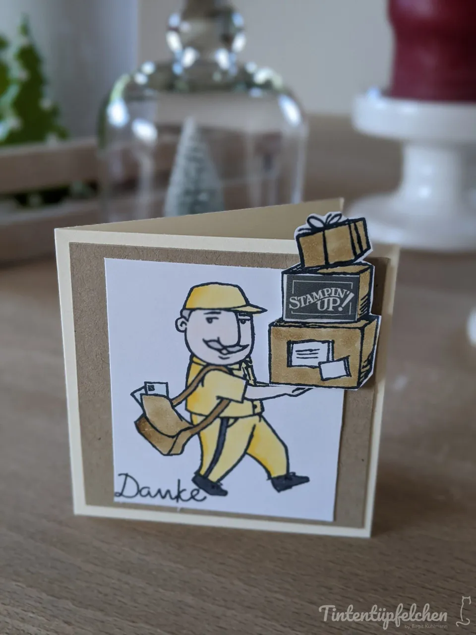 Eine Klappkarte mit einem gezeichneten Postboten in gelber Uniform, der Pakete trägt. Unter dem Motiv steht das Wort "Danke" in geschwungener Schrift.