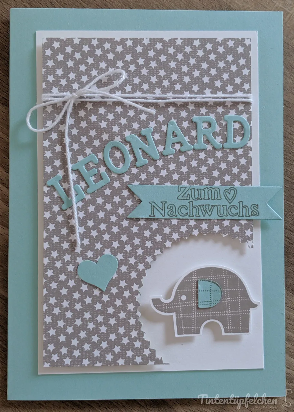 Eine Karte zur Geburt mit dem Namen "Theonard" in hellblauen Buchstaben. Ein kleiner Elefant und ein Herz sind auf einer Karte mit Sternenmuster angebracht.