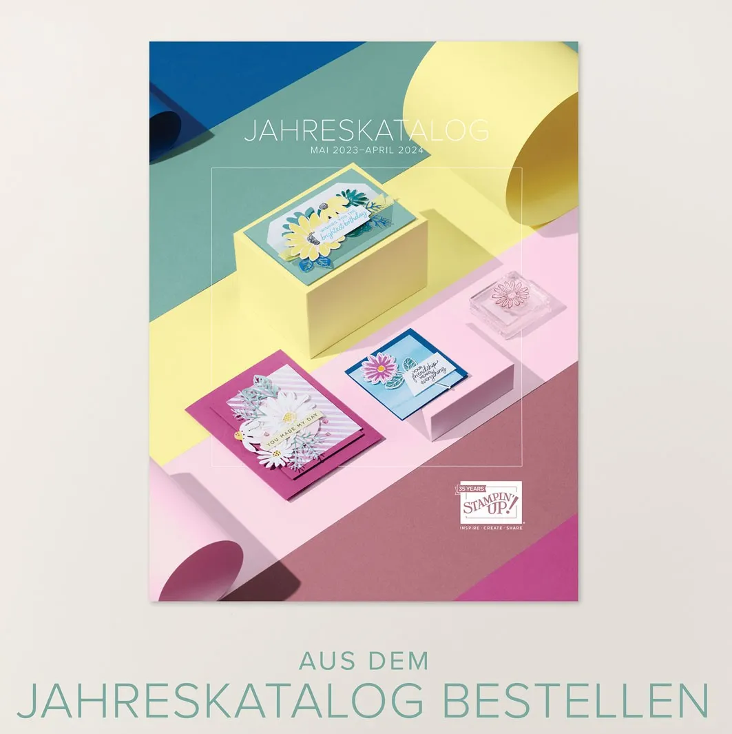 Das Cover des Stampin' Up Jahreskatalogs zeigt gestempelte Karten mit Blumenmotiven in Rosa, Blau und Gelb auf bunten Papierstufen. Der Text „JAHRESKATALOG MAI 2023–APRIL 2024“ ist oben sichtbar, unten steht „AUS DEM JAHRESKATALOG BESTELLEN“. Ein Stempel mit Blumenmuster liegt rechts neben den Karten.