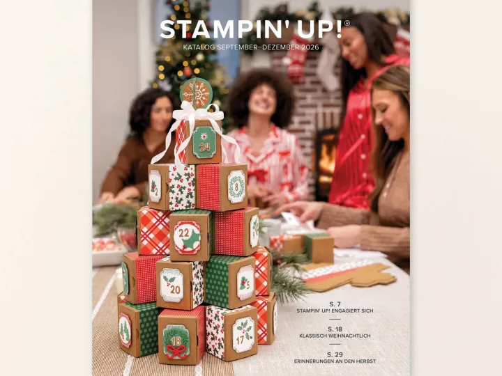 Ein Stempelkatalog für September bis Dezember 2026 zeigt eine Pyramide aus handgestempelten Adventskalender-Boxen in Rot, Grün und Braun mit Zahlen auf Etiketten. Im Hintergrund sitzen vier Frauen bei einem Tisch mit Bastelmaterial; im unscharfen Hintergrund ist ein geschmückter Weihnachtsbaum zu erkennen.