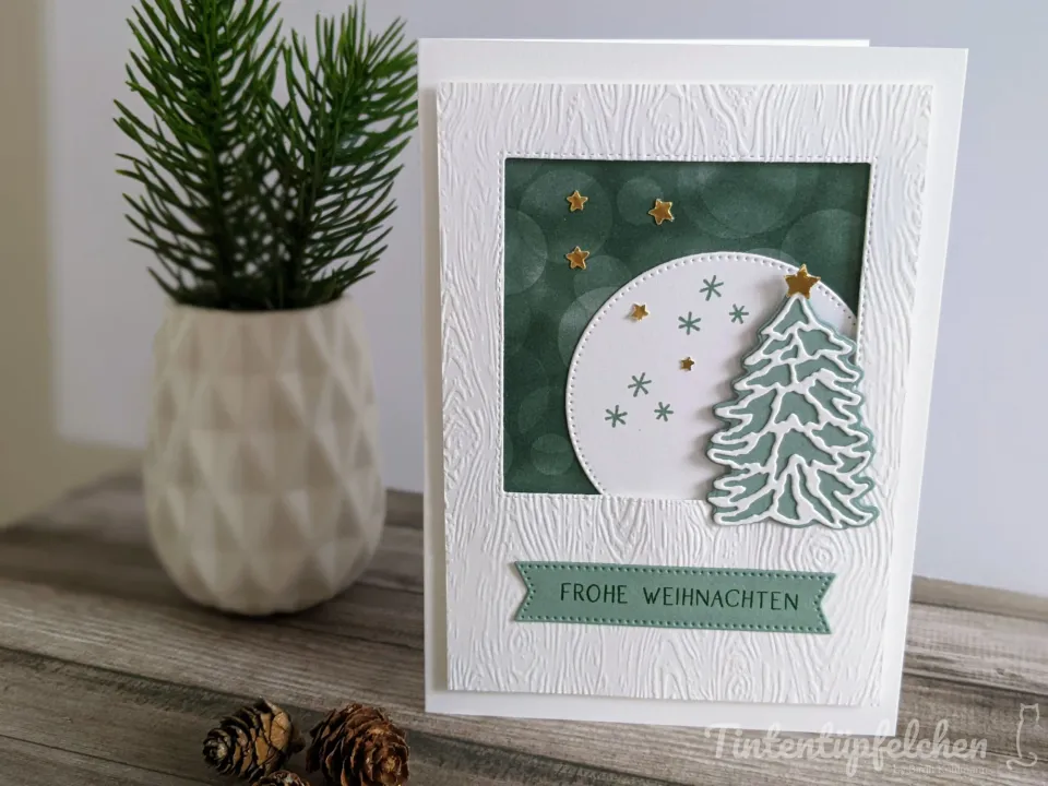 Weihnachtskarte mit gestempeltem grünen Tannenbaum und Sternen auf weißem Hintergrund, umgeben von grünem Papier mit Kreismustern. Der Text „FROHE WEIHNACHTEN" ist in einer grünen Bindeform unten angebracht.
