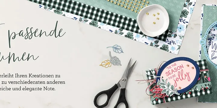 Perfekt passende Blumen: Eine Bastelcollage mit grünen und blauen Papierstücken, gestempelten Blumendetails, Scheren, einer kleinen Karte mit „Season to be Jolly“ und dekorativen Elementen auf weißem Hintergrund.