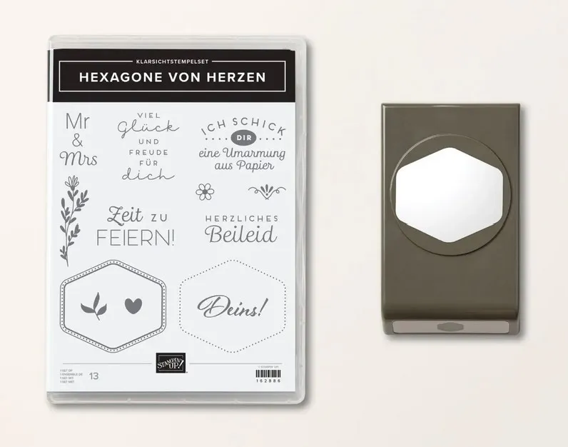 Ein Klarsichtstempelset mit den Aufschriften „Mr & Mrs“, „Viel Glück und Freude für dich“ sowie anderen Texten in verschiedenen Schriftarten, begleitet von einem Stanzrahmen in grauer Farbe mit einem sechseckigen Ausschnitt. Das Set enthält auch grafische Elemente wie eine Pflanze, ein Herz und dekorative Linien.