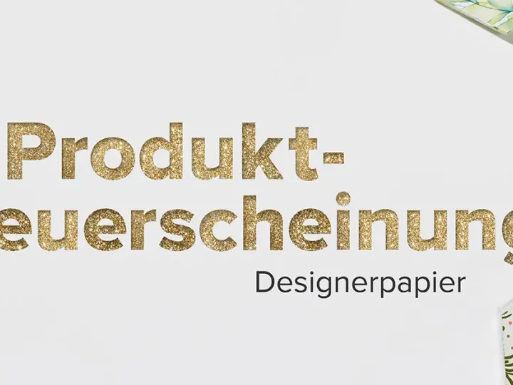 Goldener Text „Produkt-Neuerscheinung Designerpapier" steht zentral auf weißem Hintergrund. Um ihn herum sind hexagonale Papierstücke in verschiedenen Mustern und Farben angeordnet: glänziges Gold, mattes Silber, pastellrosa mit Wasserfarbton, grüne Blätter, rote Motive von Äpfeln sowie ein Muster mit Teebechern und Sternen. Die Hexagone zeigen unterschiedliche Texturen wie Glitter oder Druckmuster.