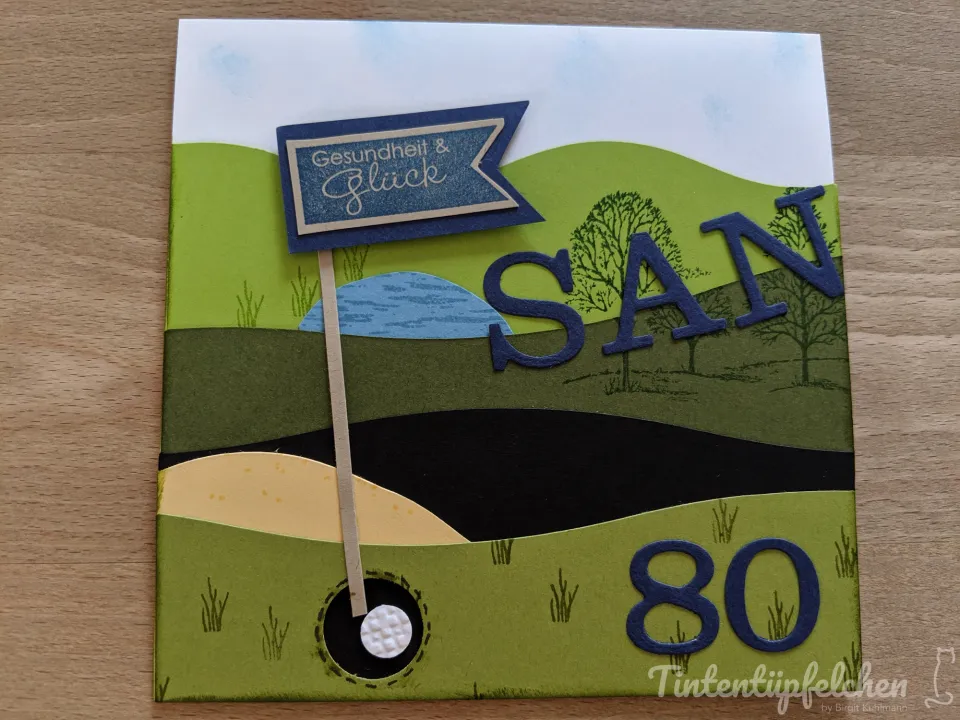 Eine Karte mit Golfmotiv, auf der "Gesundheit & Glück" und der Name "SAN" zu lesen sind. Die Zahl 80 ist ebenfalls auf der Karte angebracht.
