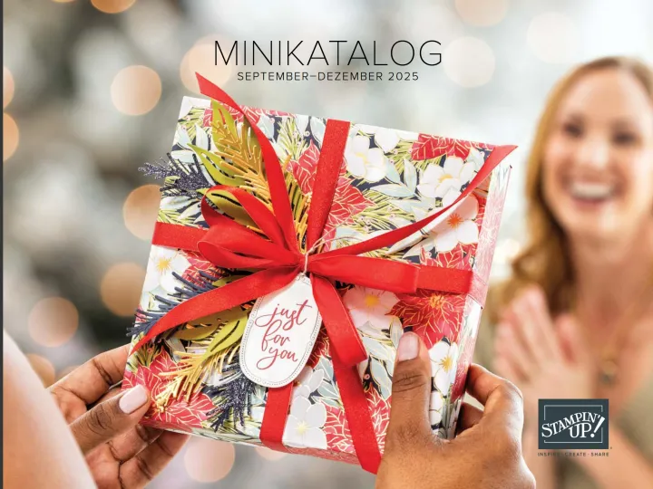 Ein geschenkverpacktes Kasten mit floraler Musterung in Rot, Weiß und Grün ist mit rotem Seidenband gebunden und verziert mit gestempelten Tannenzweigen. Eine weiße Aufkleber-Tag zeigt die Aufschrift „just for you" in kalligrafischer Schrift. Im Hintergrund steht eine lächelnde Frau vor einem verschwommenen Weihnachtsbaum.