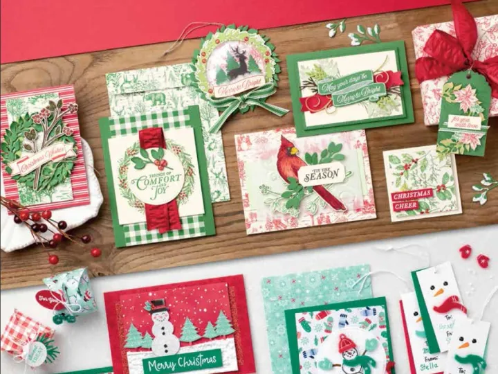 Einige Weihnachtskarten und Geschenkanhänger mit Schneemännern, Tannenzweigen und roten Schleifen sind auf einem Holztisch arrangiert. Ein rotes Cover mit dem Schriftzug "Die Kreativität ruft!" und dem Stampin' Up!-Logo ist im oberen Bereich zu sehen.